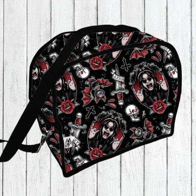 Mochila pequena preta com padrão de caveiras, morcegos, rosas e figura de mulher em fundo de madeira clara