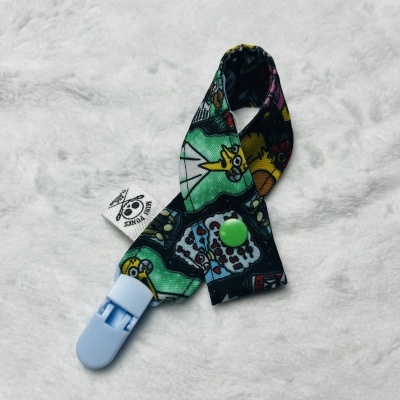 Prendedor colorido com padrão cartoon e clipe azul sobre fundo branco felpudo.