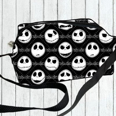 Mala preta com padrão de caveiras brancas e alça preta sobre chão de madeira