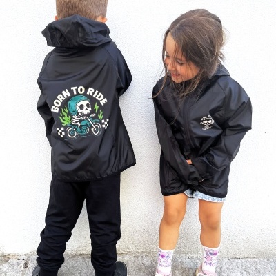 Crianças a usar casacos impermeáveis pretos com estampas e capuz, em frente a parede branca.