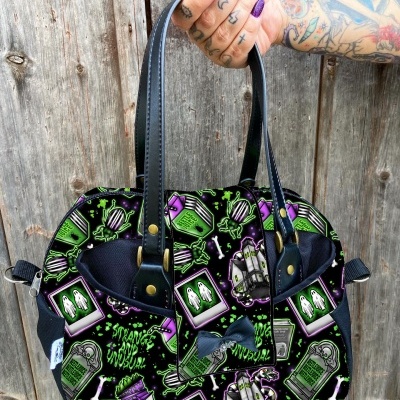 Bolsa preta com estampado colorido de Halloween segurada por mão tatuada.