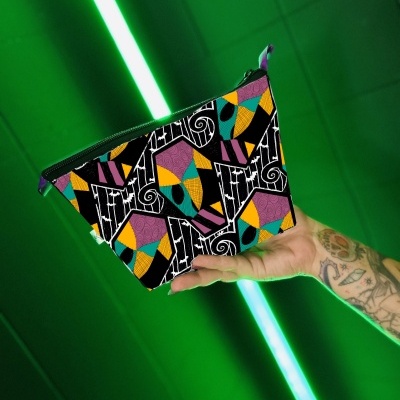 Bolsa pequena colorida com padrão geométrico segurada por mão tatuada em fundo verde