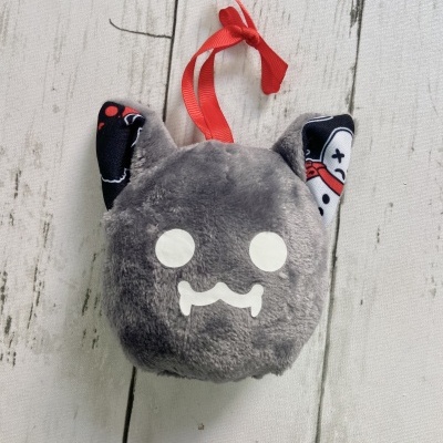 Pelúcia cinzenta com rosto branco e orelhas pretas decoradas pendurada numa fita vermelha sobre fundo de madeira clara