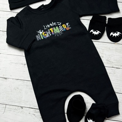 Conjunto de bebé preto com padrão Little NIGHTMARE e acessórios temáticos em fundo de madeira branca