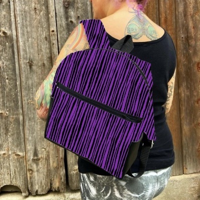 Mochila roxa estampada com riscas pretas usada por pessoa com tatuagens em fundo de porta de madeira