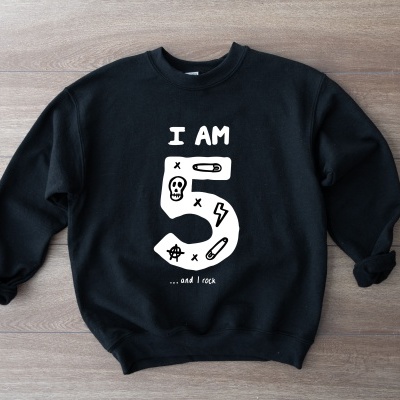 Sweatshirt preta com texto e desenhos brancos colocada sobre superfície de madeira.