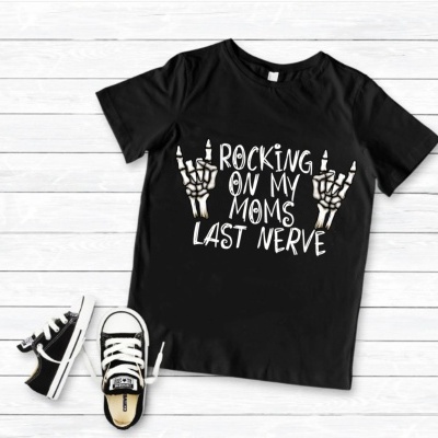 T-shirt preta com texto e mãos em gesto rock, e ténis preto e branco num chão de madeira clara.