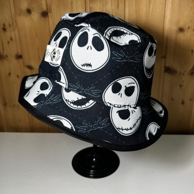 Chapéu bucket preto com padrão de caveiras brancas em fundo de madeira