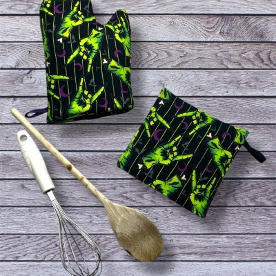 Utensílios de cozinha em tecido estampado com luva térmica, pega para forno, colher de pau e batedor sobre madeira.