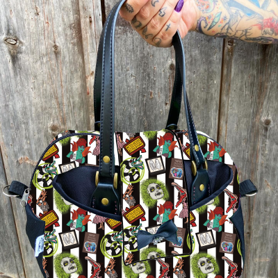 Mala colorida com vários padrões gráficos e alças pretas, segurada por mão tatuada