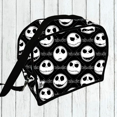 Mala preta com padrão de rostos brancos sobre fundo de madeira clara