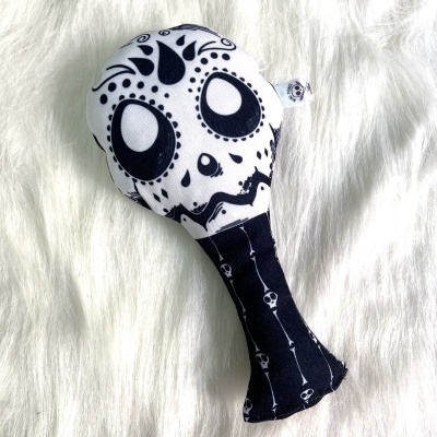 Brinquedo de tecido preto e branco com estampa de caveira decorativa colocado sobre superfície branca fofa