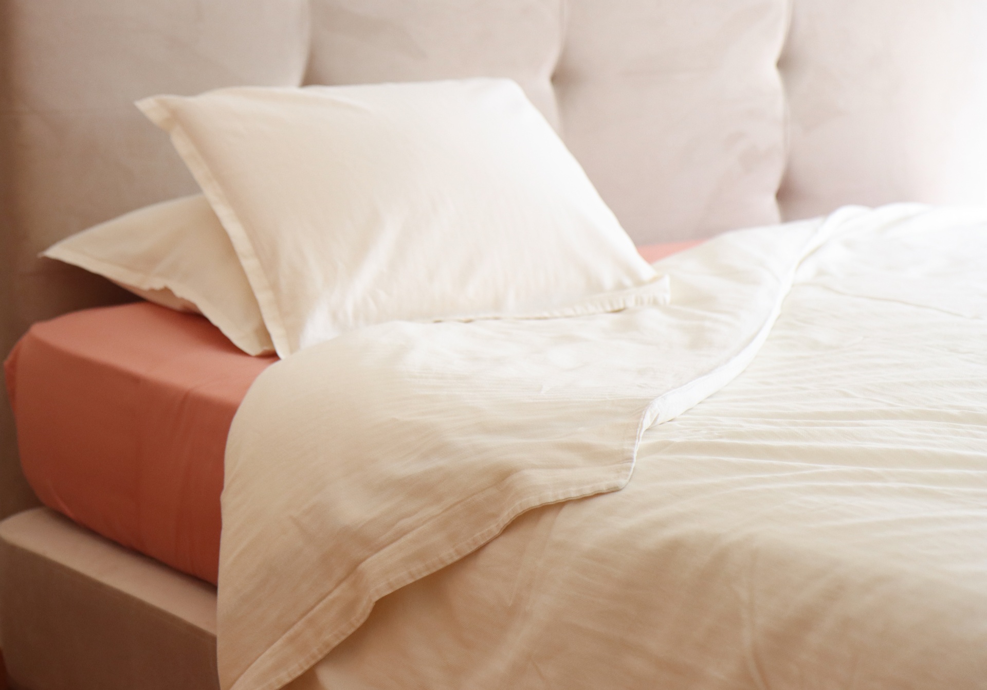 Cama com lençol laranja, almofadas creme e manta leve creme