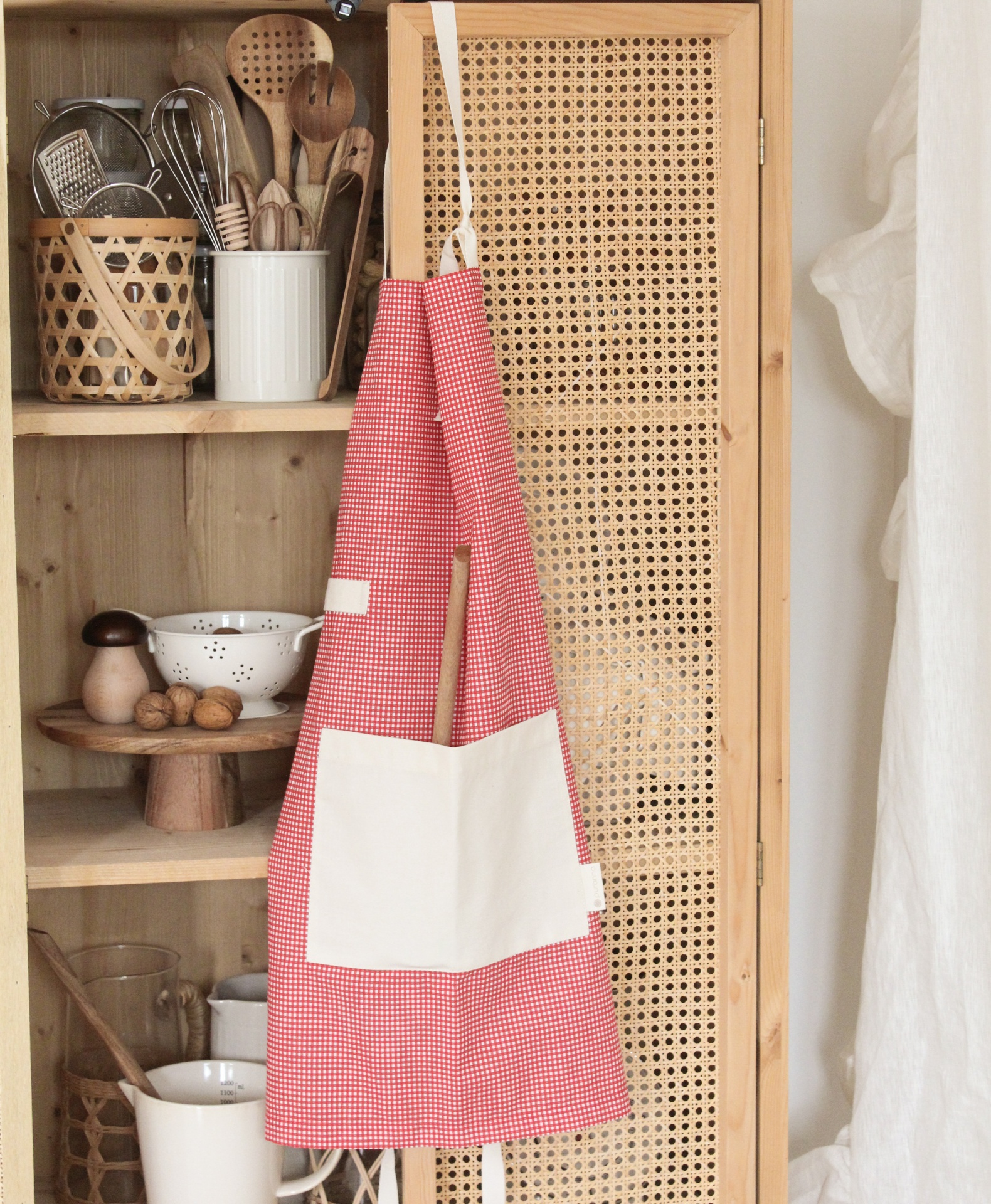 Avental vermelho com bolso branco pendurado em armário de palhinha