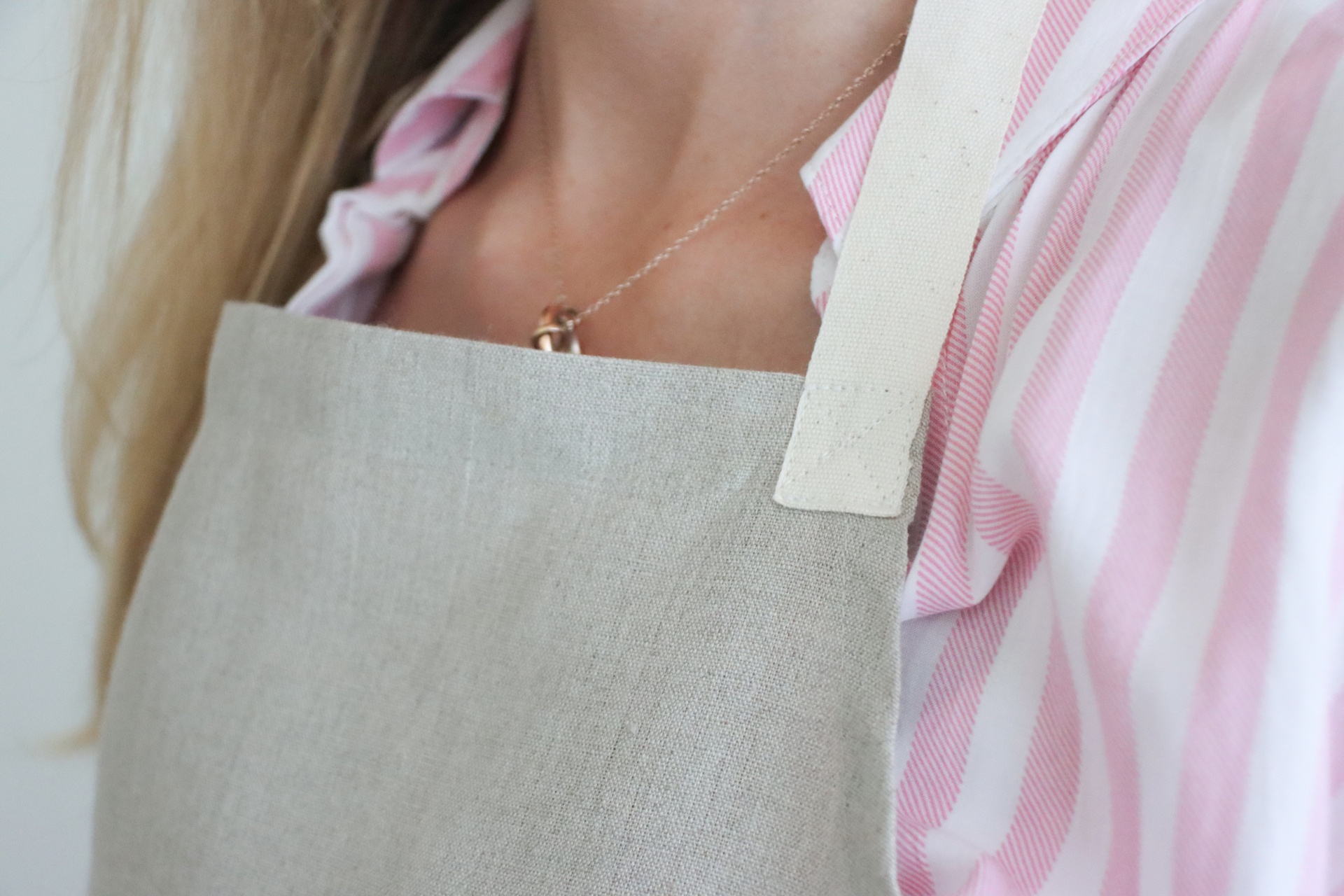 Avental cinzento claro com alças brancas usado sobre camisa rosa às riscas brancas