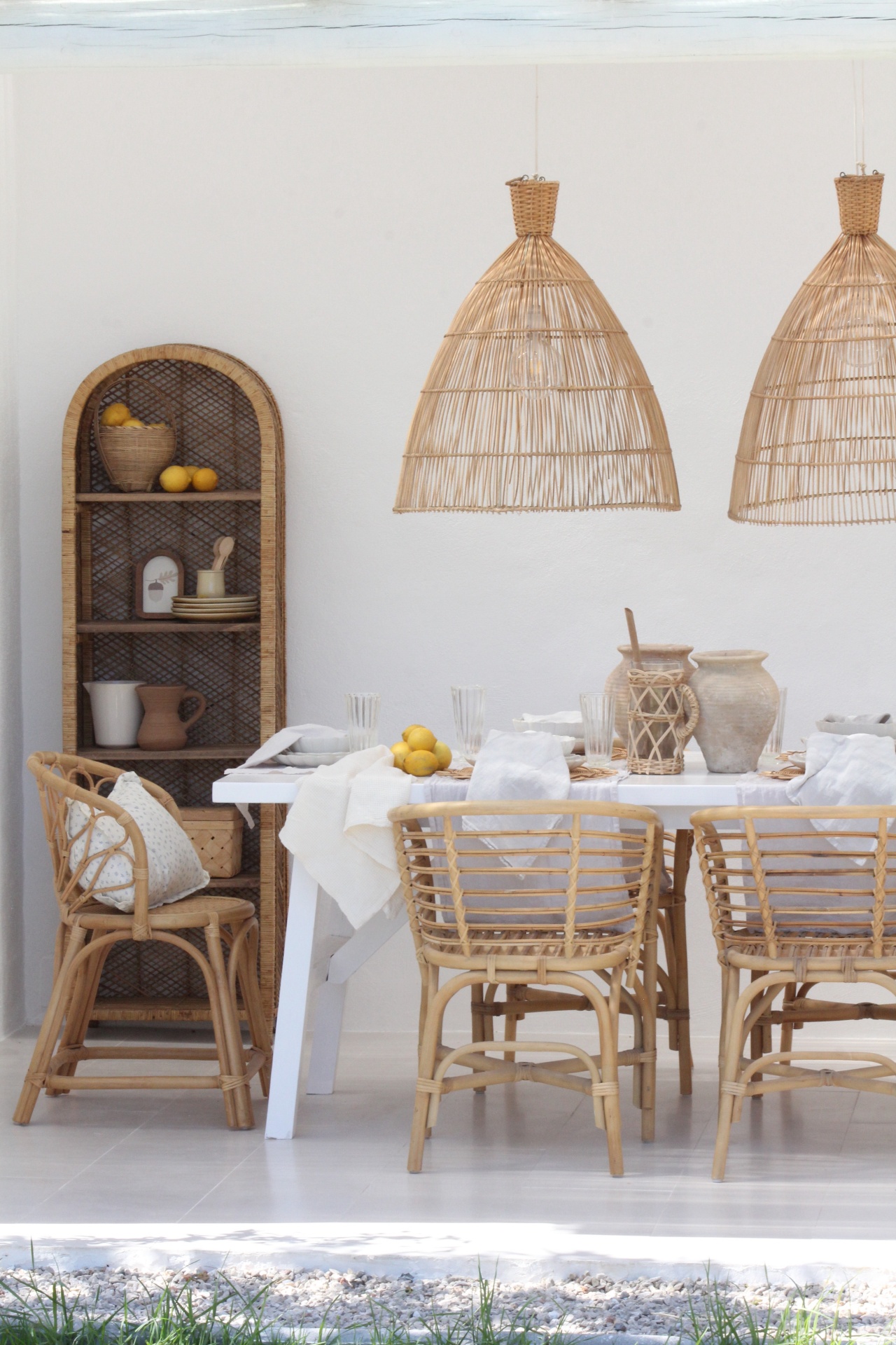 Mesa de jantar branca com cadeiras de vime e luminárias pendentes de vime em sala com estante alta de madeira