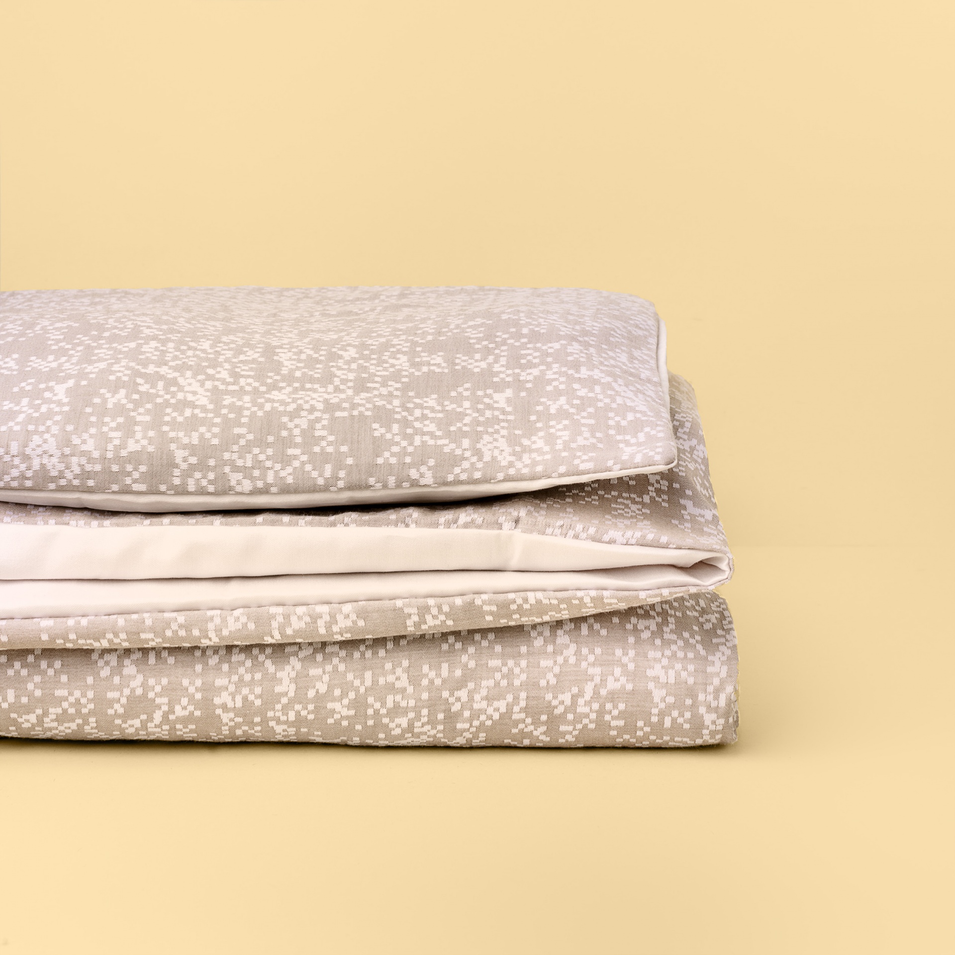 Conjunto de roupa de cama bege com padrão branco dobrado sobre superfície creme