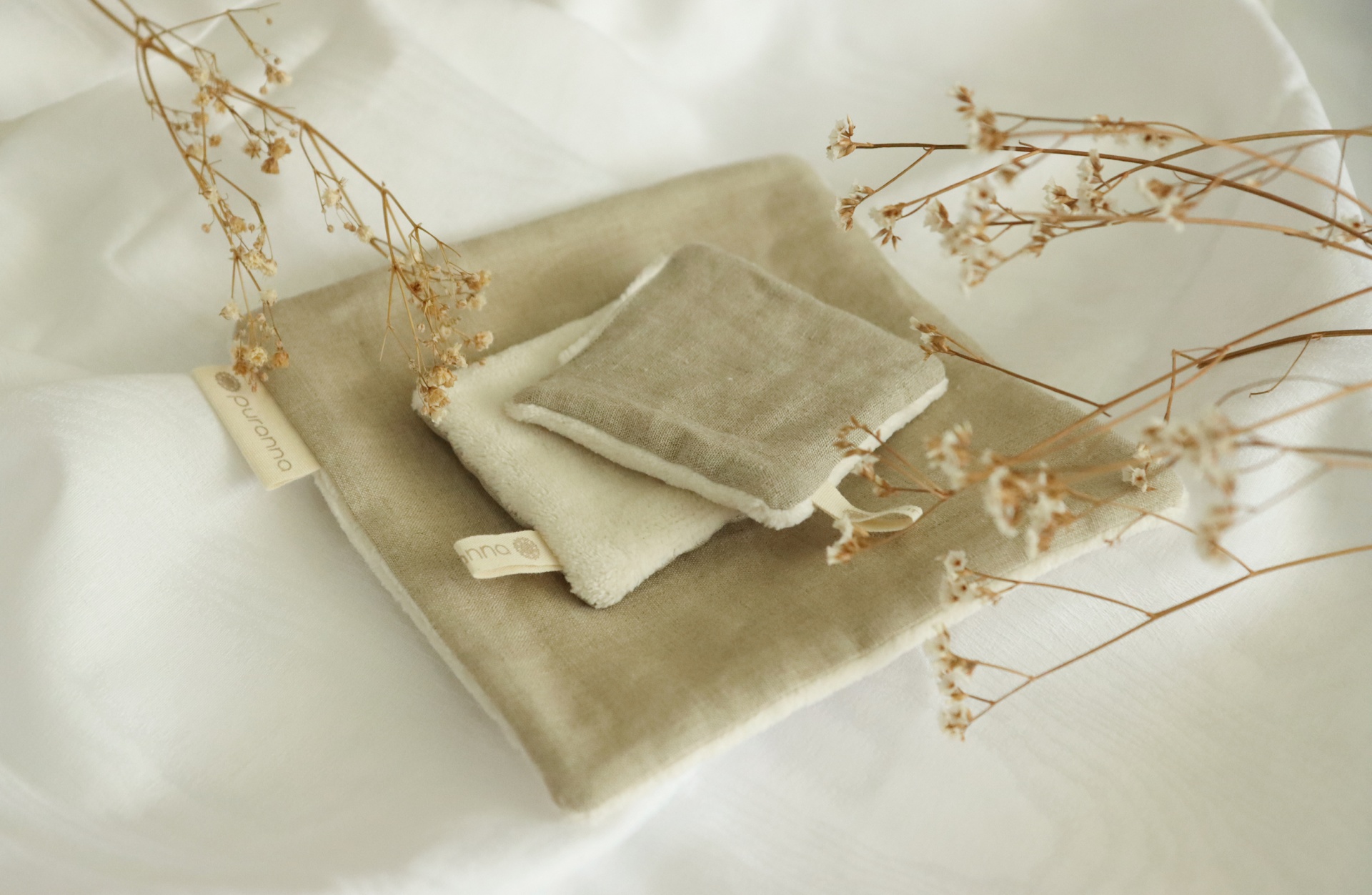 Três panos de tecido neutros com raminhos secos sobre tecido branco.