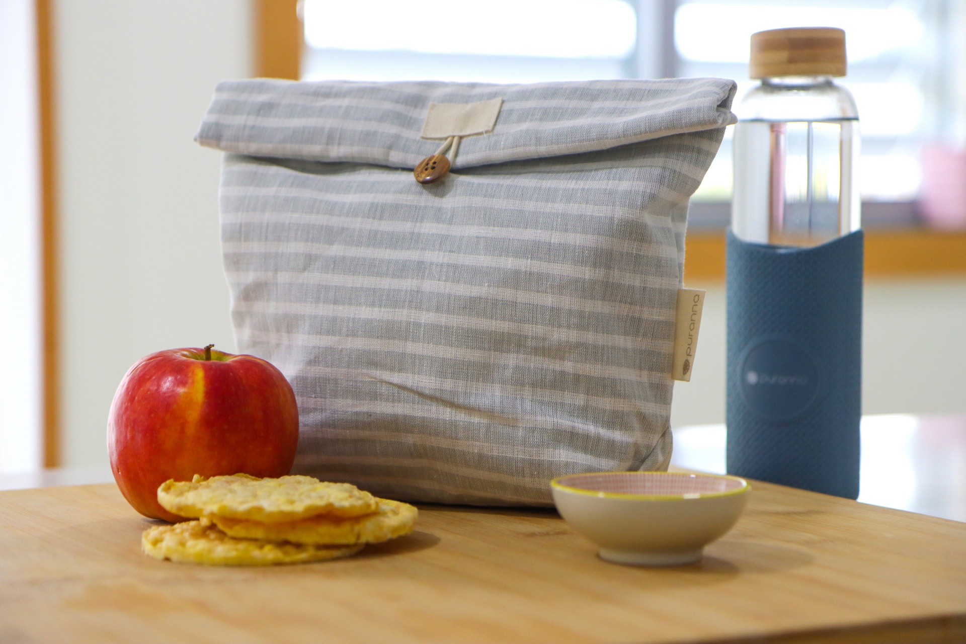 Marmita cinzenta riscada, garrafa de vidro com tampa, maçã vermelha, bolachas e recipiente de cerâmica sobre mesa de madeira