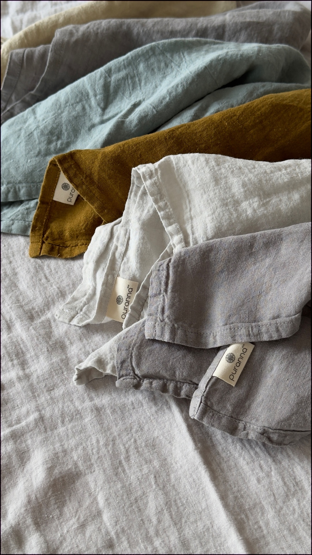Tecidos coloridos com etiquetas 'purannq' sobre tecido cinza claro.