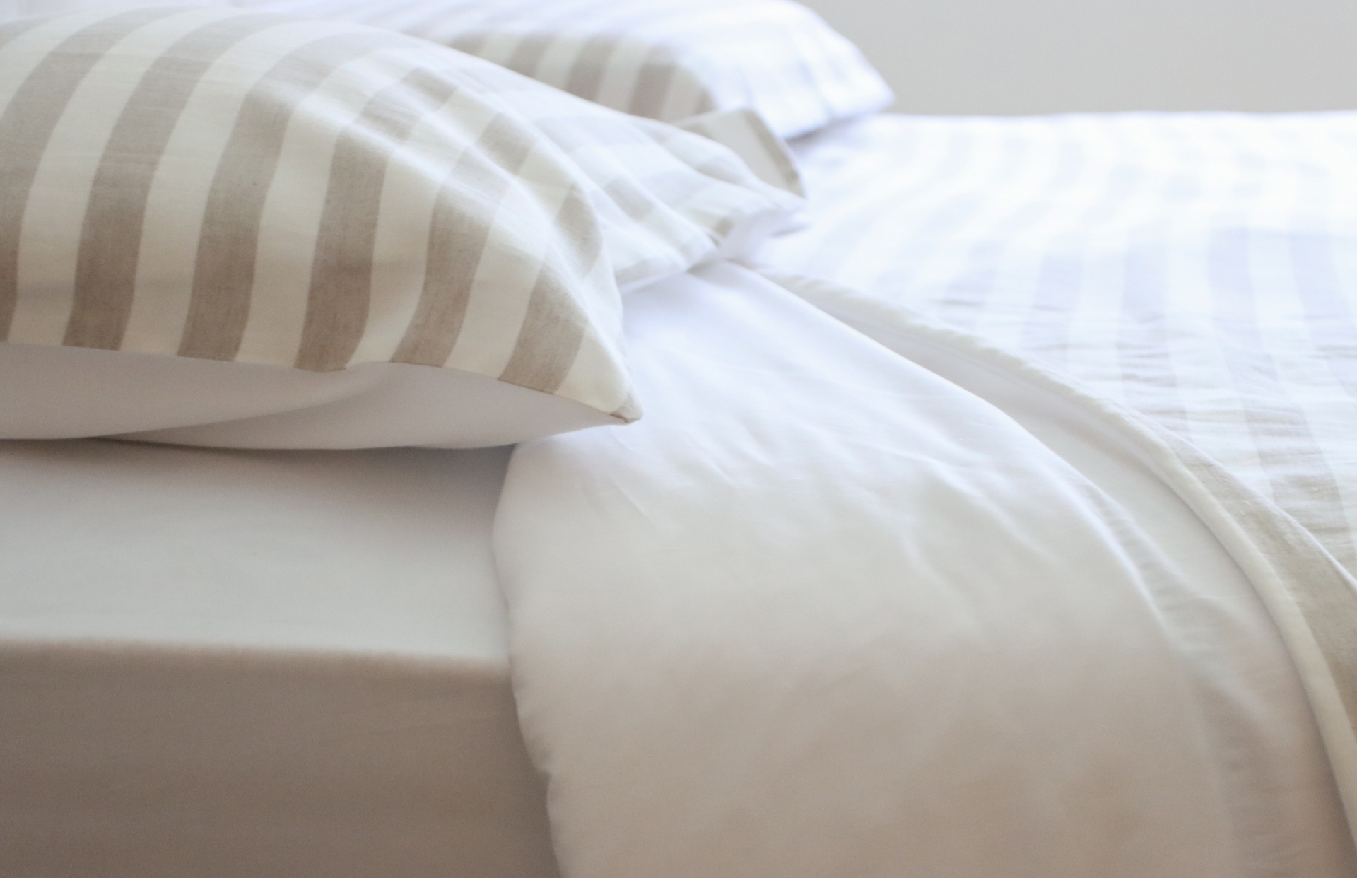 Cama com lençol branco e almofadas de riscas cinzentas