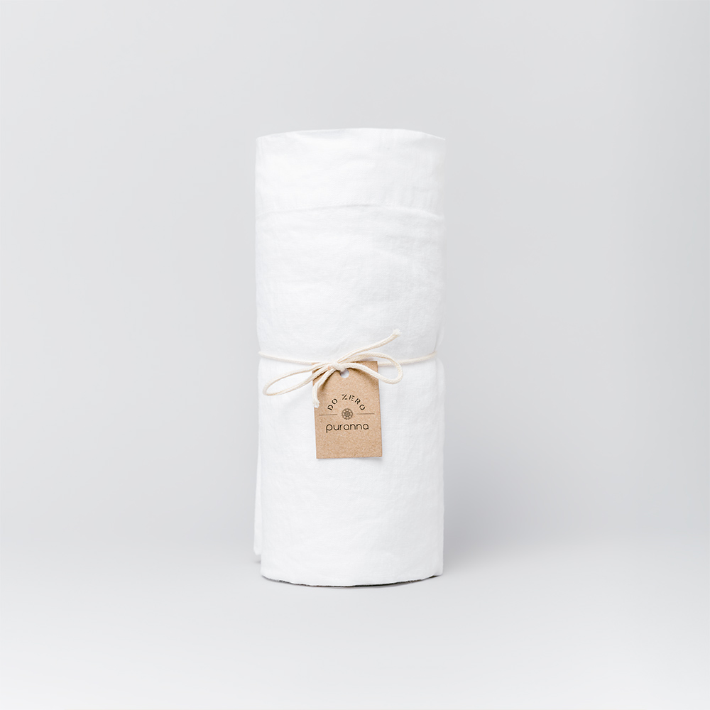 Toalha branca enrolada com etiqueta Puranna em fundo branco