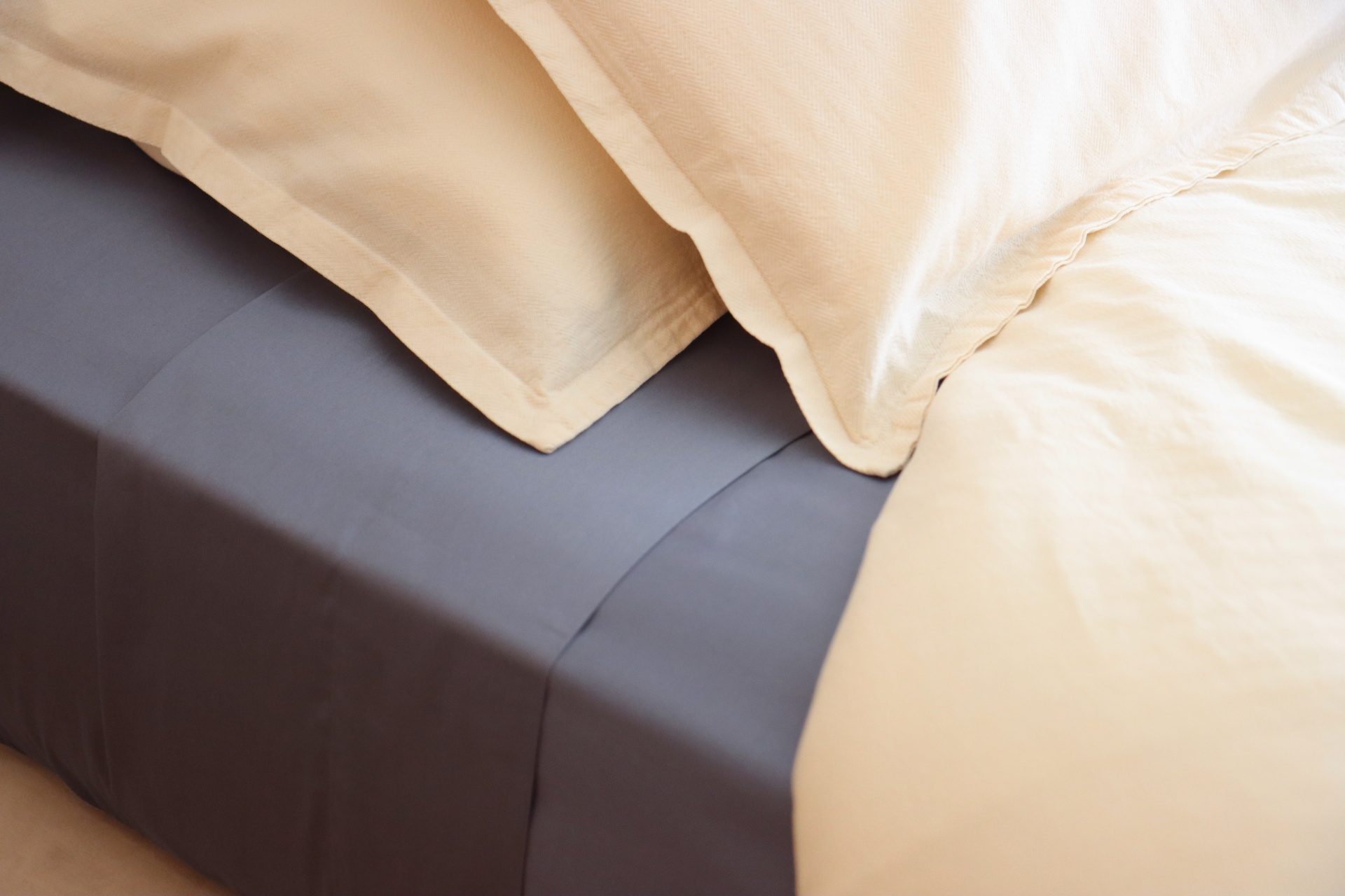 Colchão com lençol cinzento escuro e almofadas amarelas claras