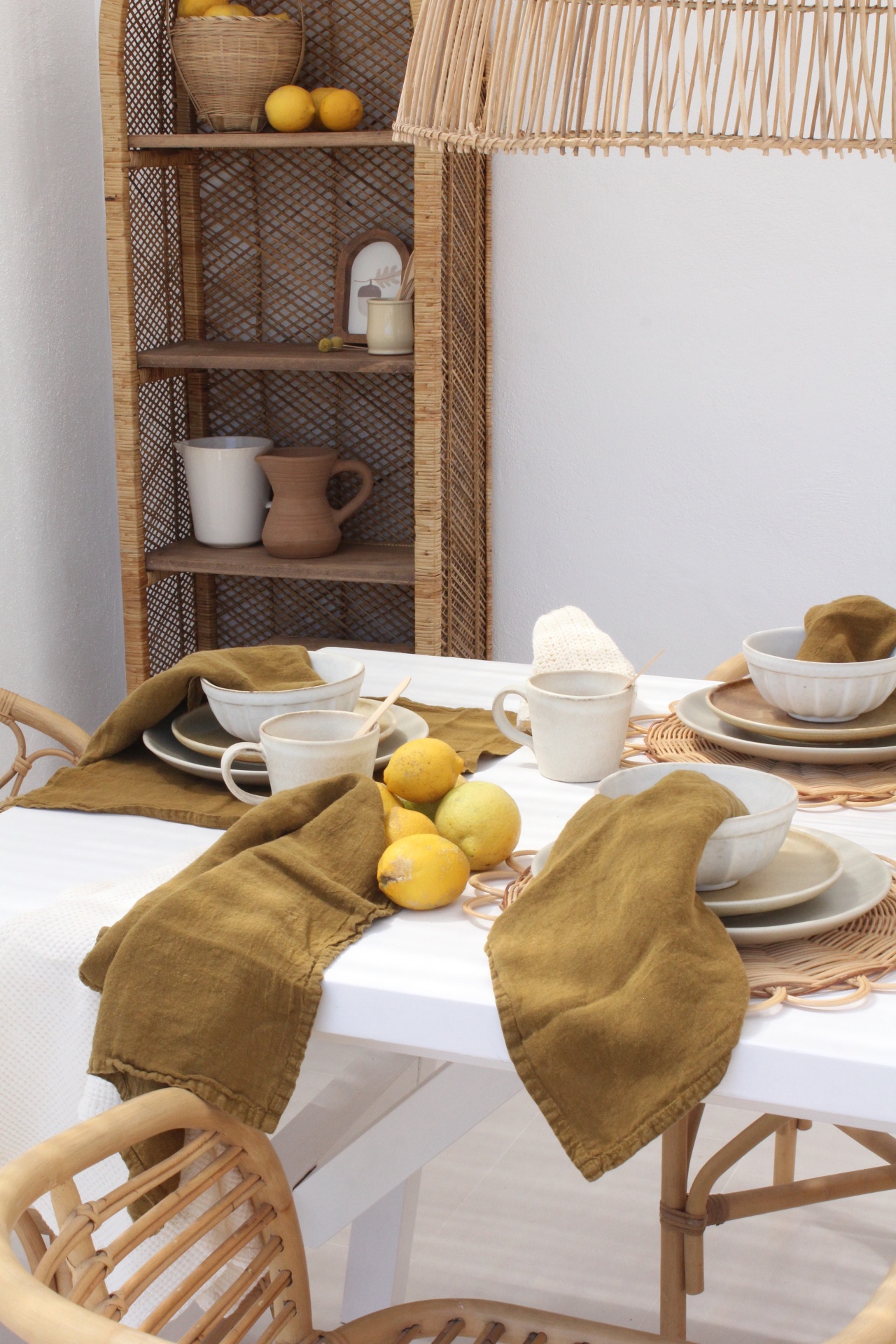 Mesa de jantar com loiça creme e castanha, guardanapos castanhos e limões, cadeiras e estante de vime