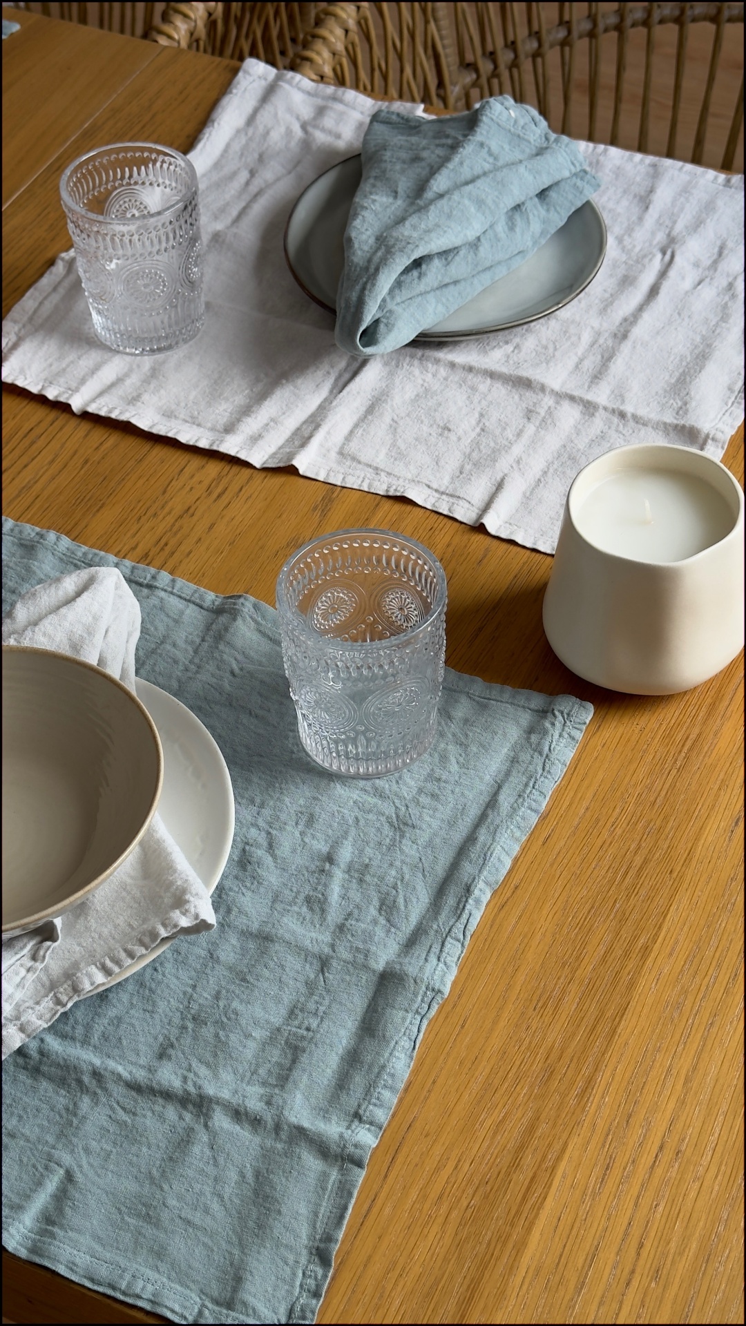 Mesa de madeira posta com pratos, tigelas, copos de vidro, guardanapos de linho e vela cerâmica
