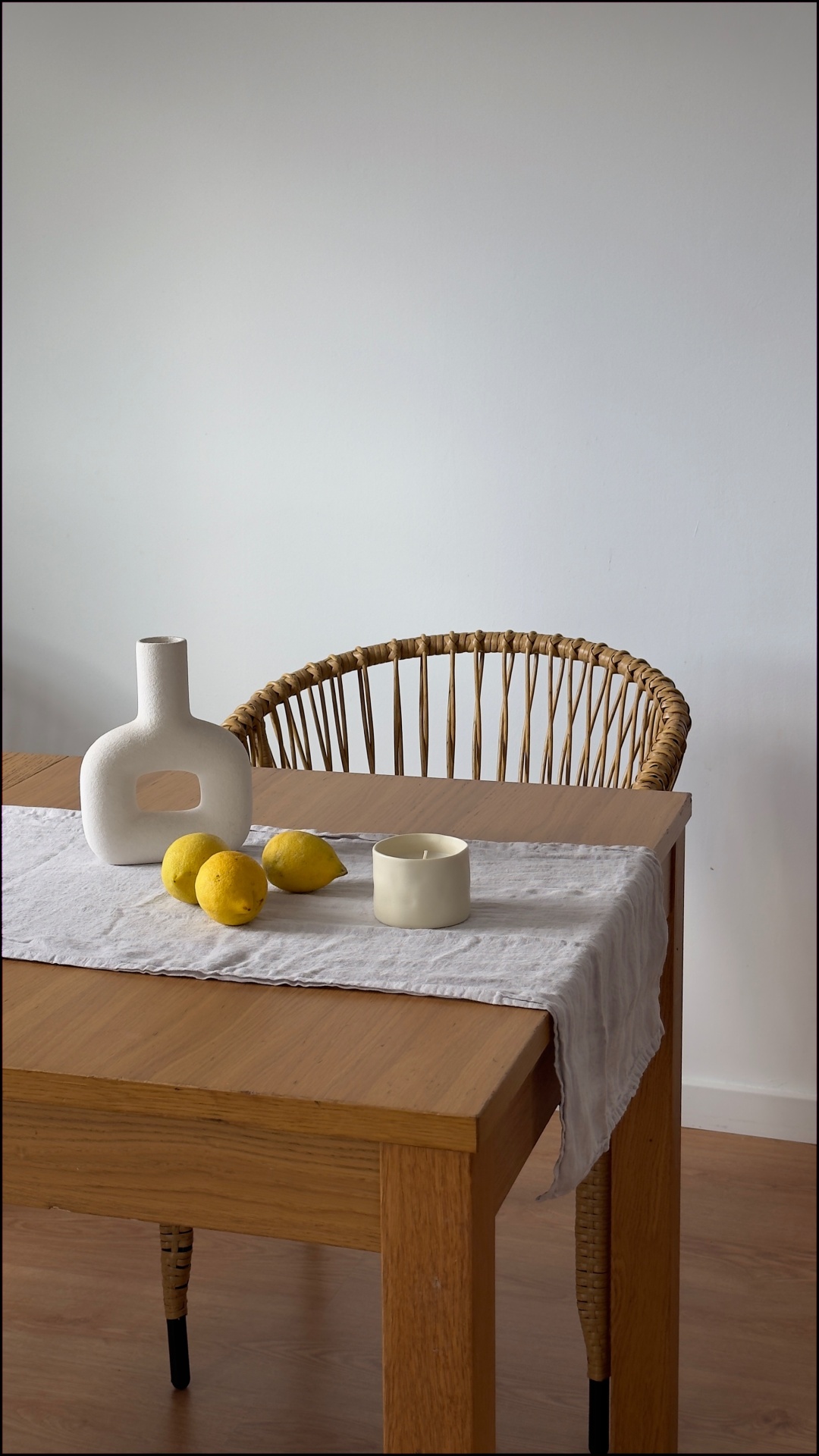 Mesa de madeira com vaso branco, vela, limões e cadeira de rato natural