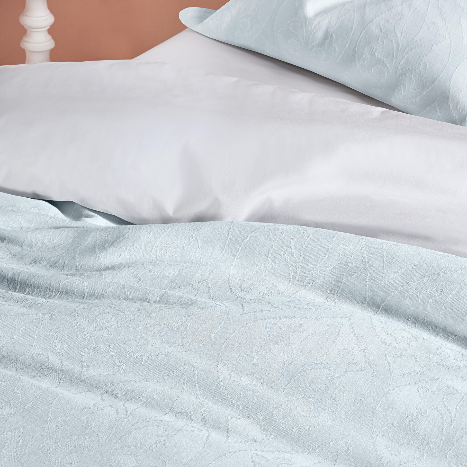 Roupa de cama com lençol branco e colcha azul clara com padrão floral