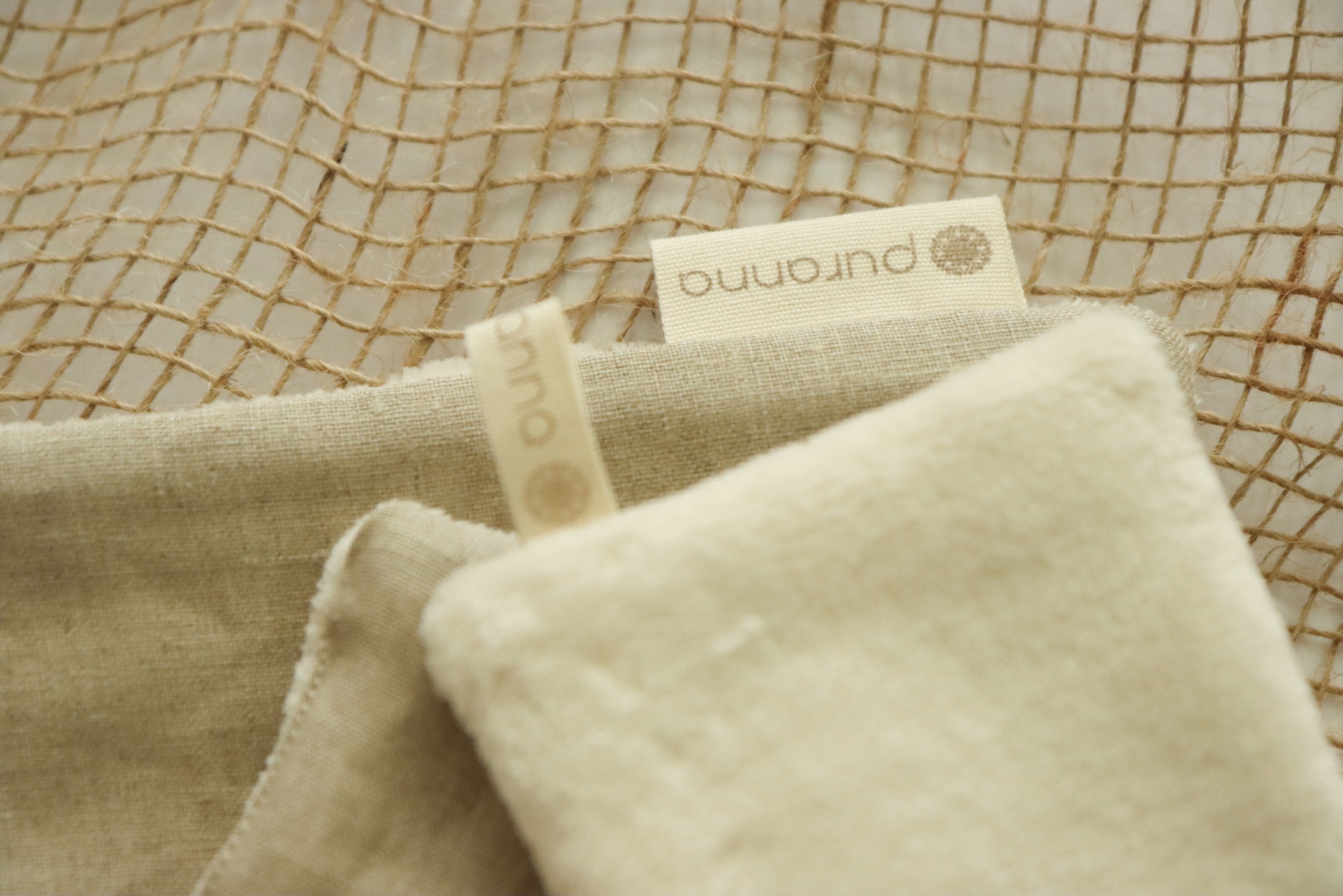 Três panos neutros com etiquetas 'puranna' sobre rede bege