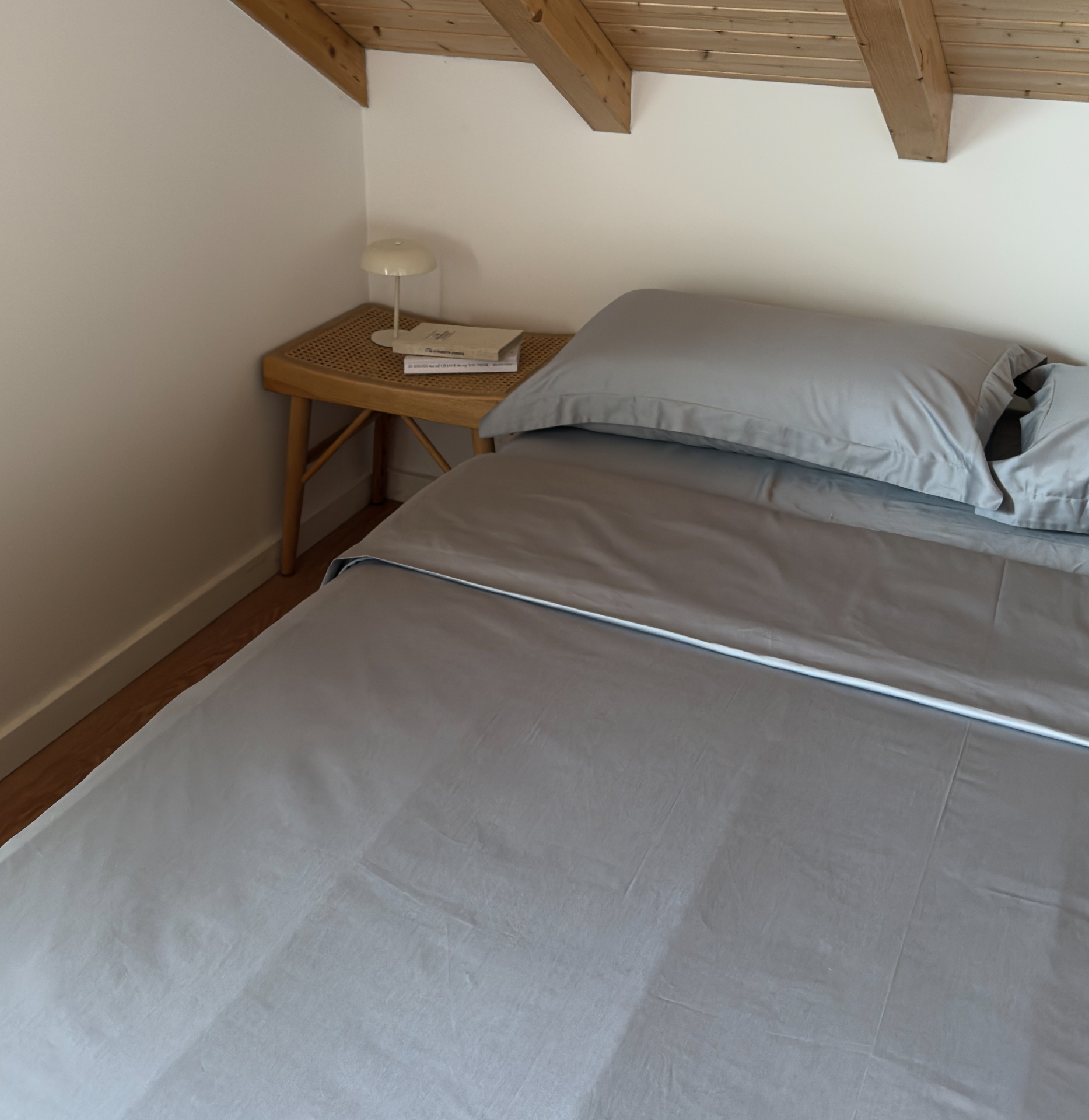 Cama com roupa de cama cinza clara e mesa de cabeceira em madeira clara