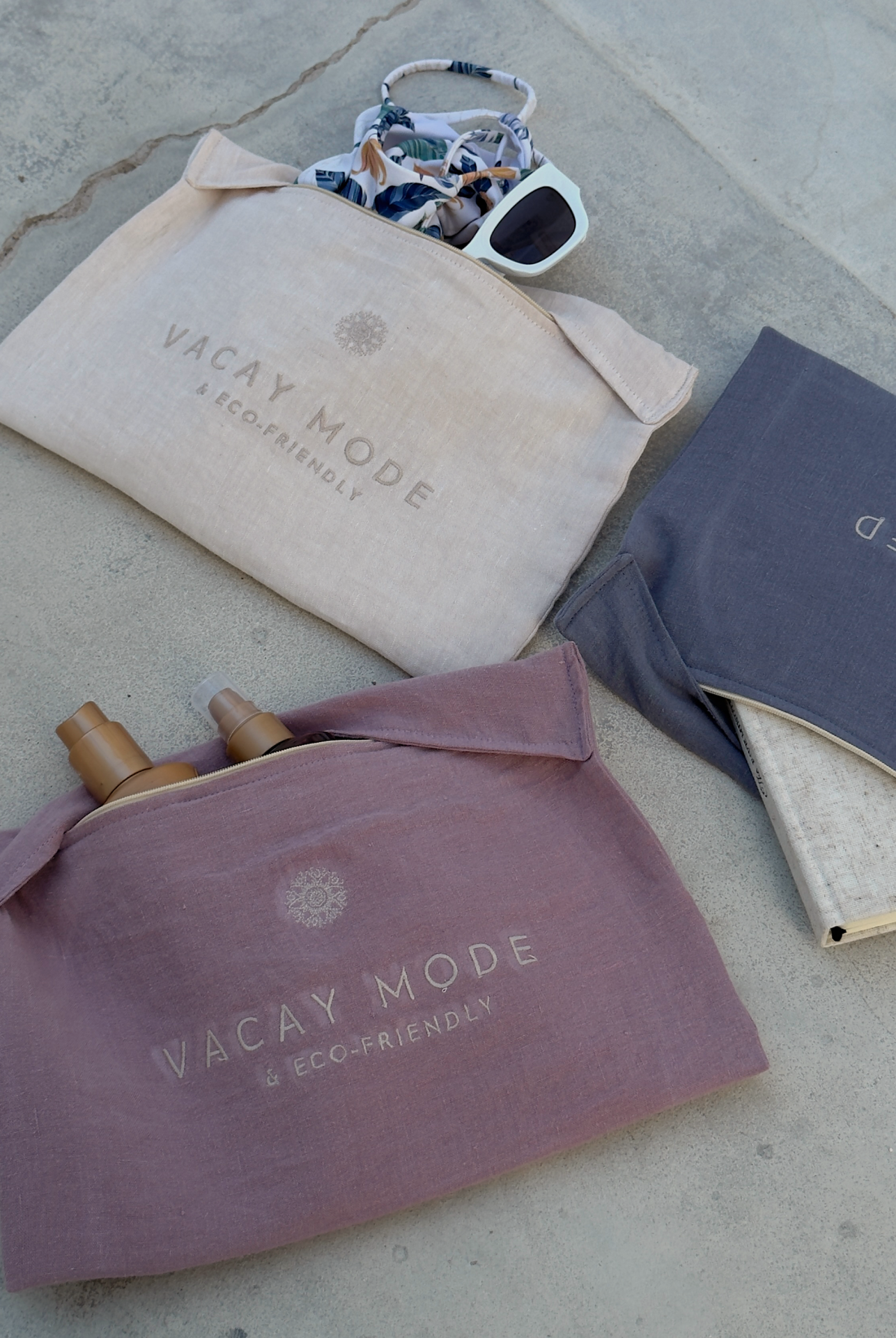 Três bolsas de tecido com texto VACAY MODE ECO-FRIENDLY e acessórios como óculos de sol e protetores solares