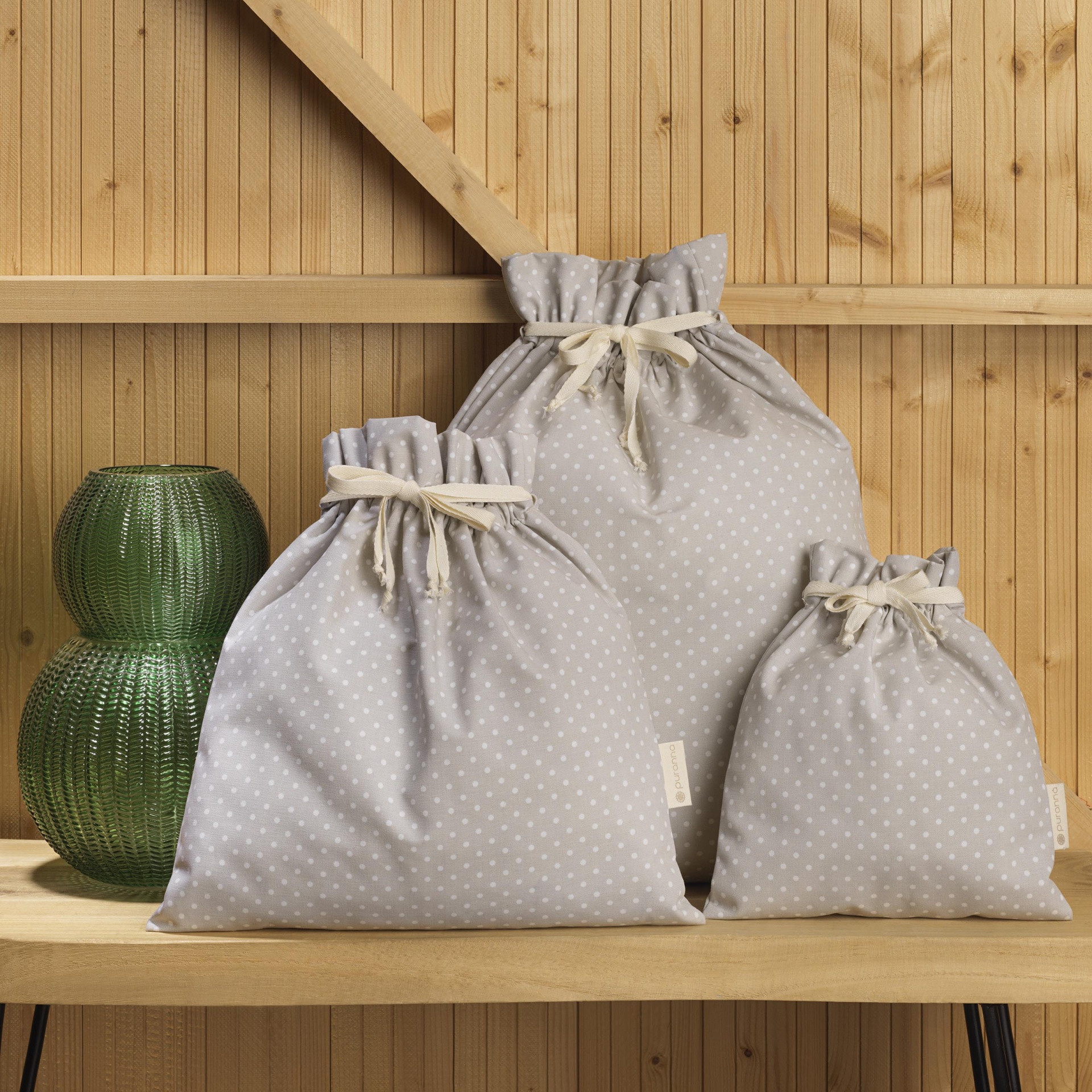 Três sacos de tecido cinzento com pontos brancos e cordão de fecho em madeira clara