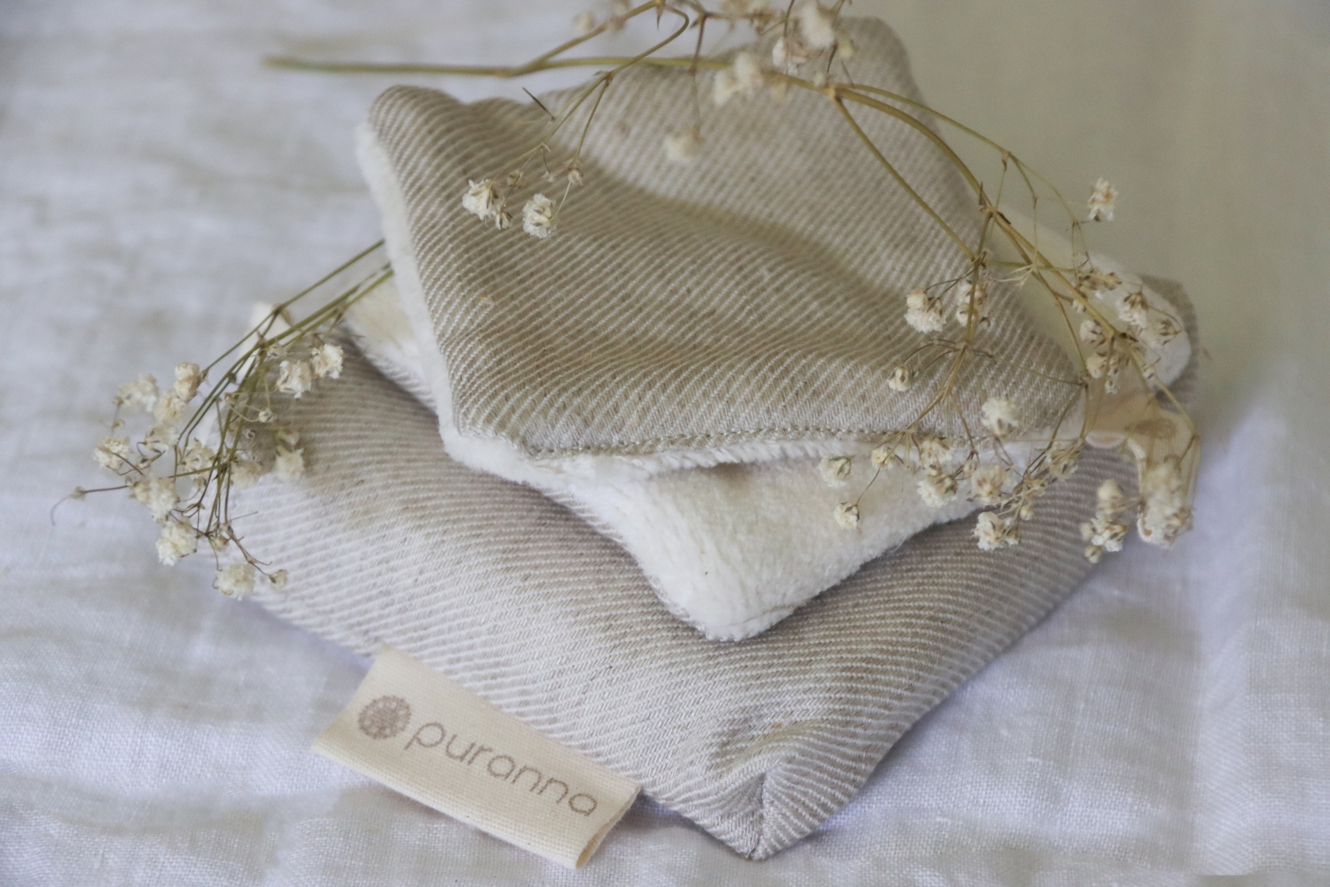 Toalhas ou panos macios empilhados com flores secas e etiqueta 'puranna'