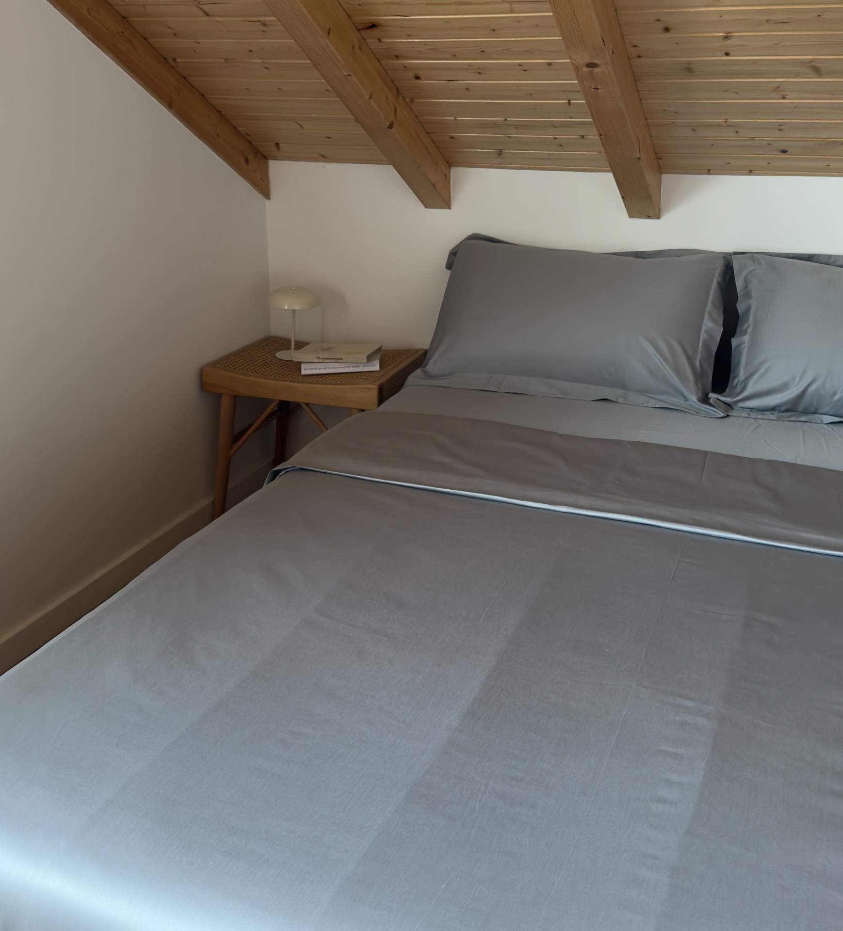 Cama com roupa de cama cinzenta e mesa de cabeceira de madeira