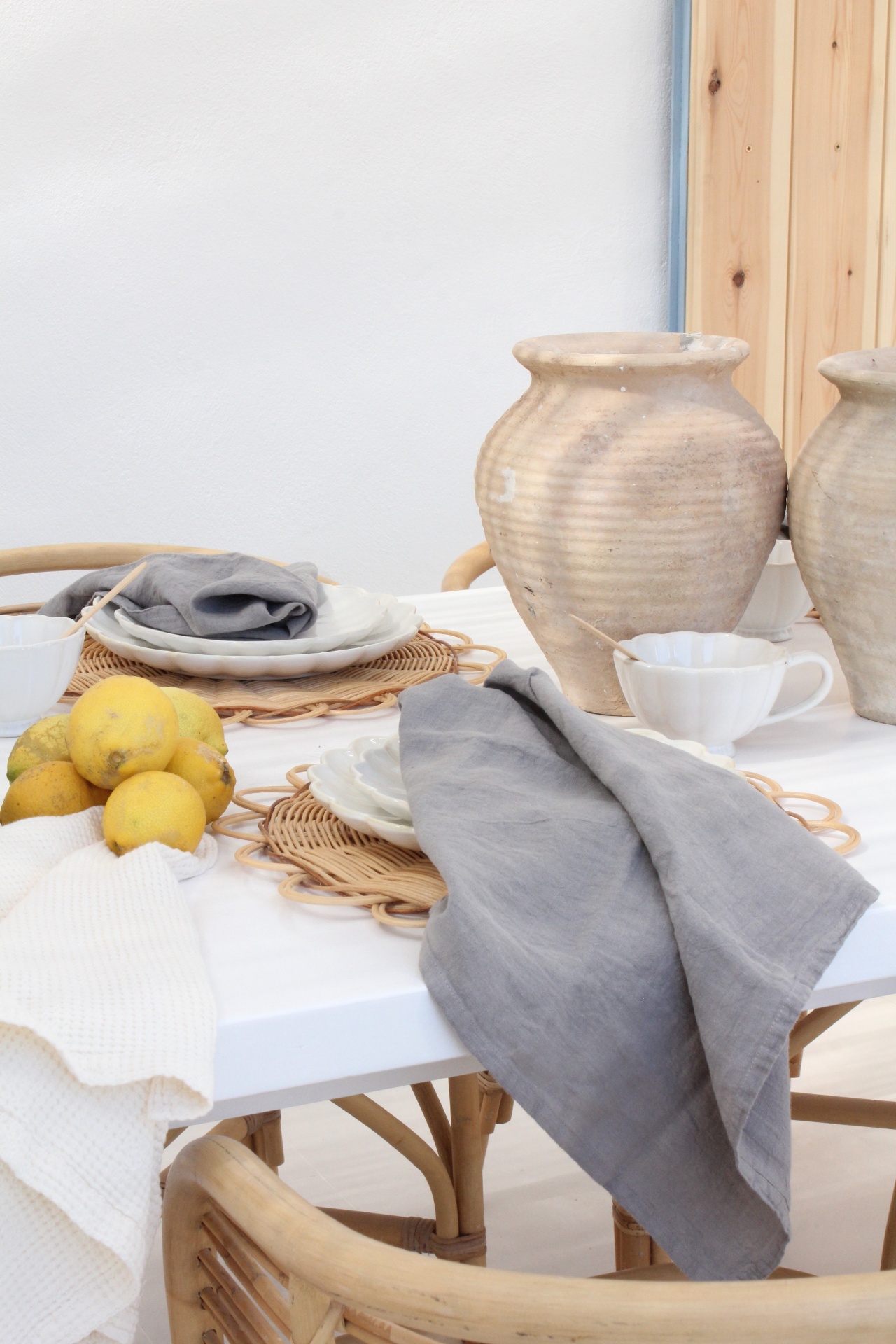 Mesa branca decorada com pratos, toalhas de linho, jarros de cerâmica e limões.