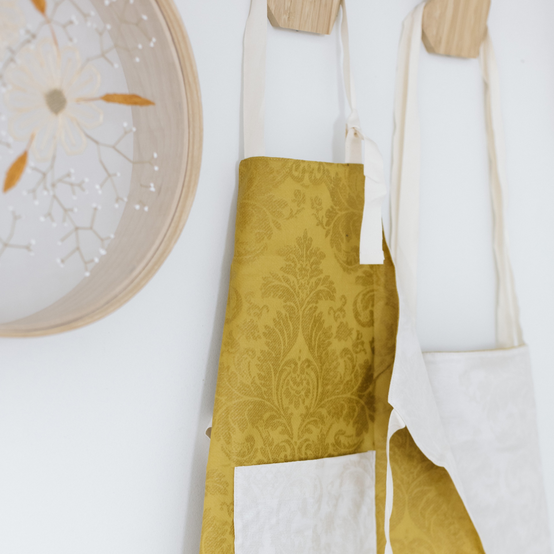 Dois aventais pendurados em parede branca com prato decorativo ao lado