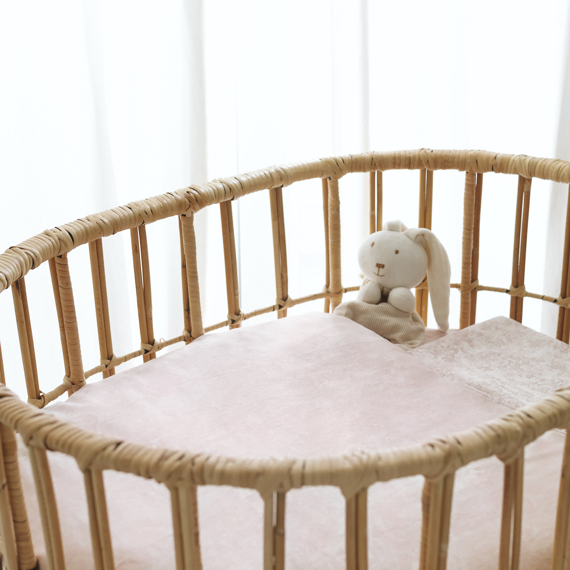 Berço de rattan natural com colchão rosa e peluche de coelho branco