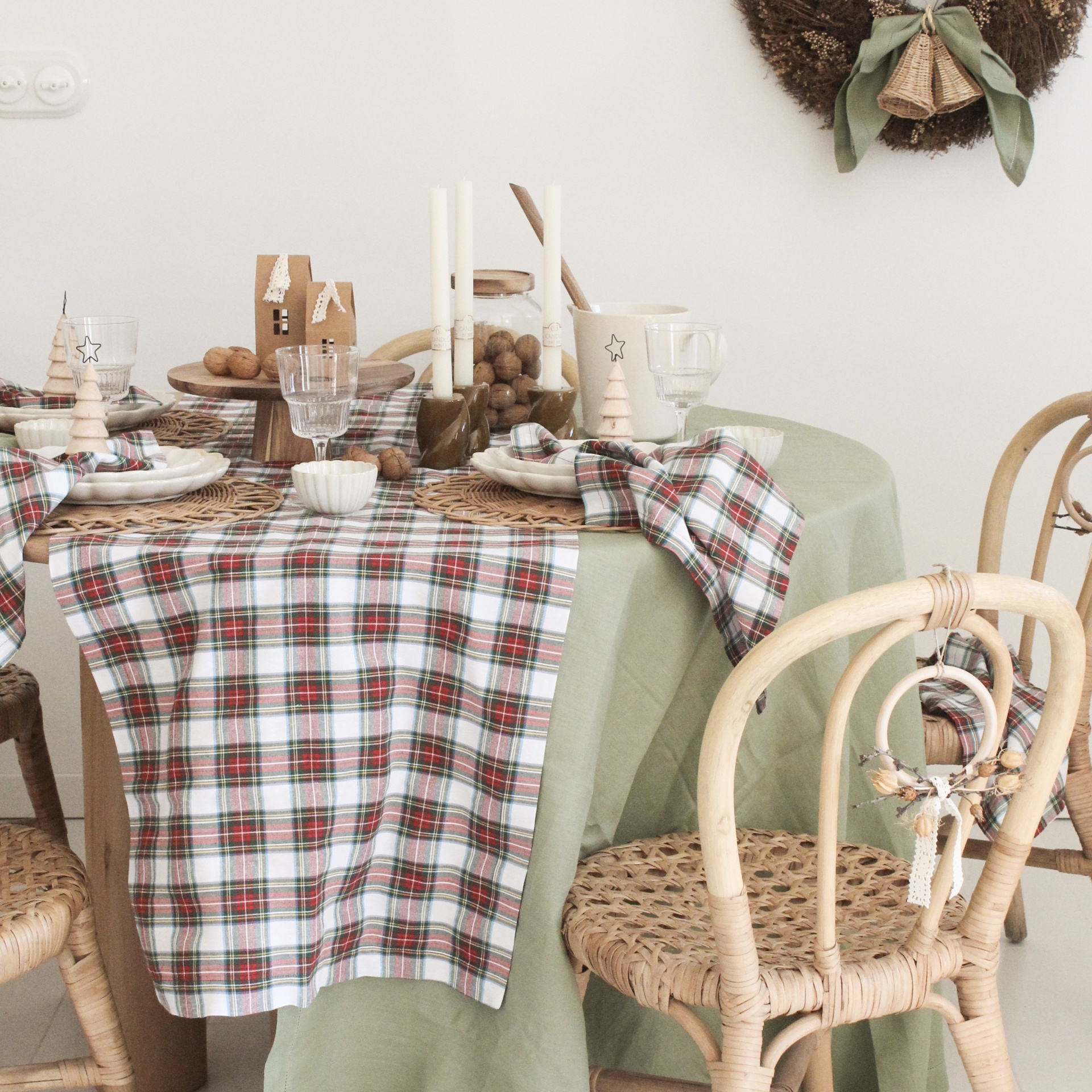Mesa de jantar decorada com toalha verde e xadrez, velas brancas e cadeiras de rattan