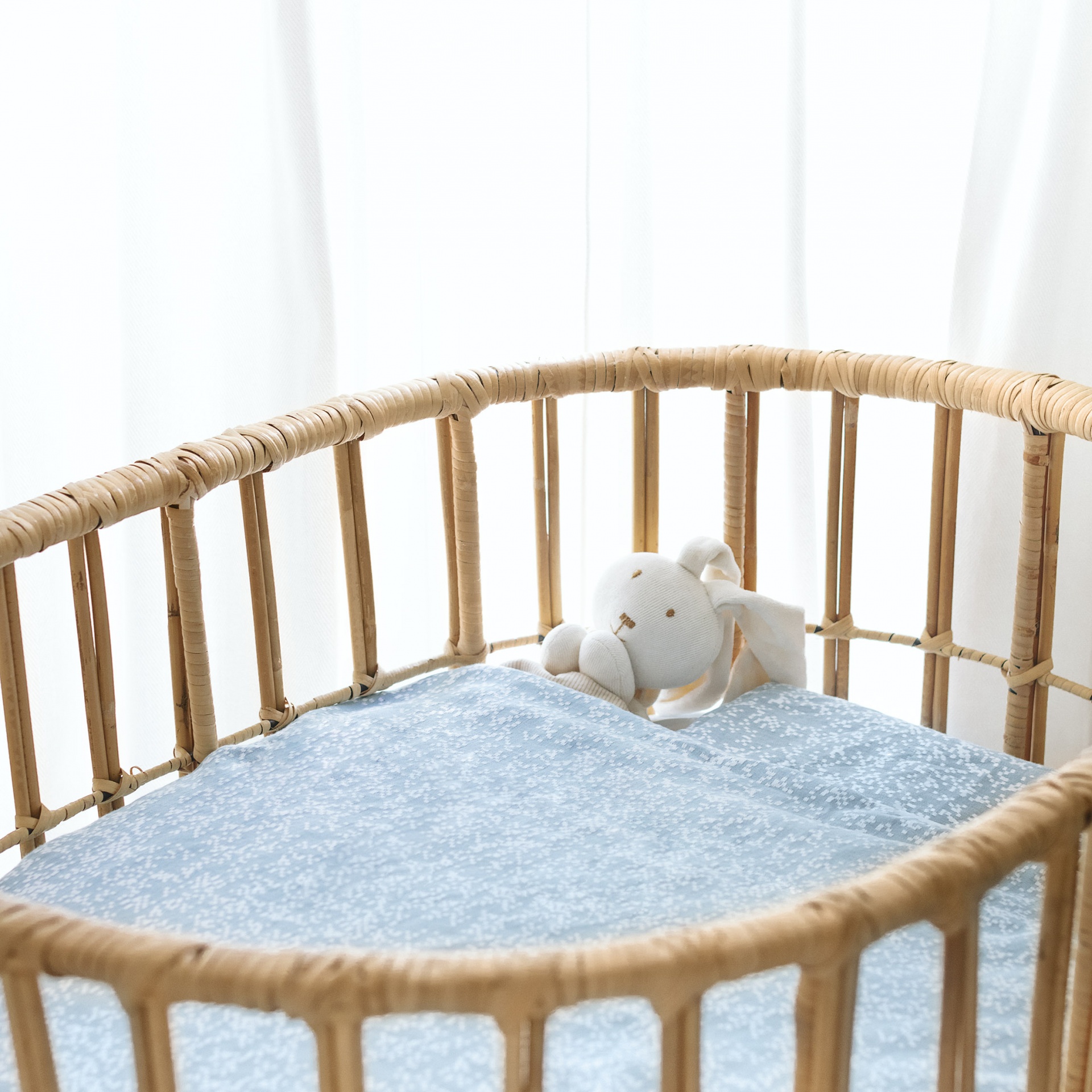 Berço oval de rattan com colchão azul claro e coelho de peluche