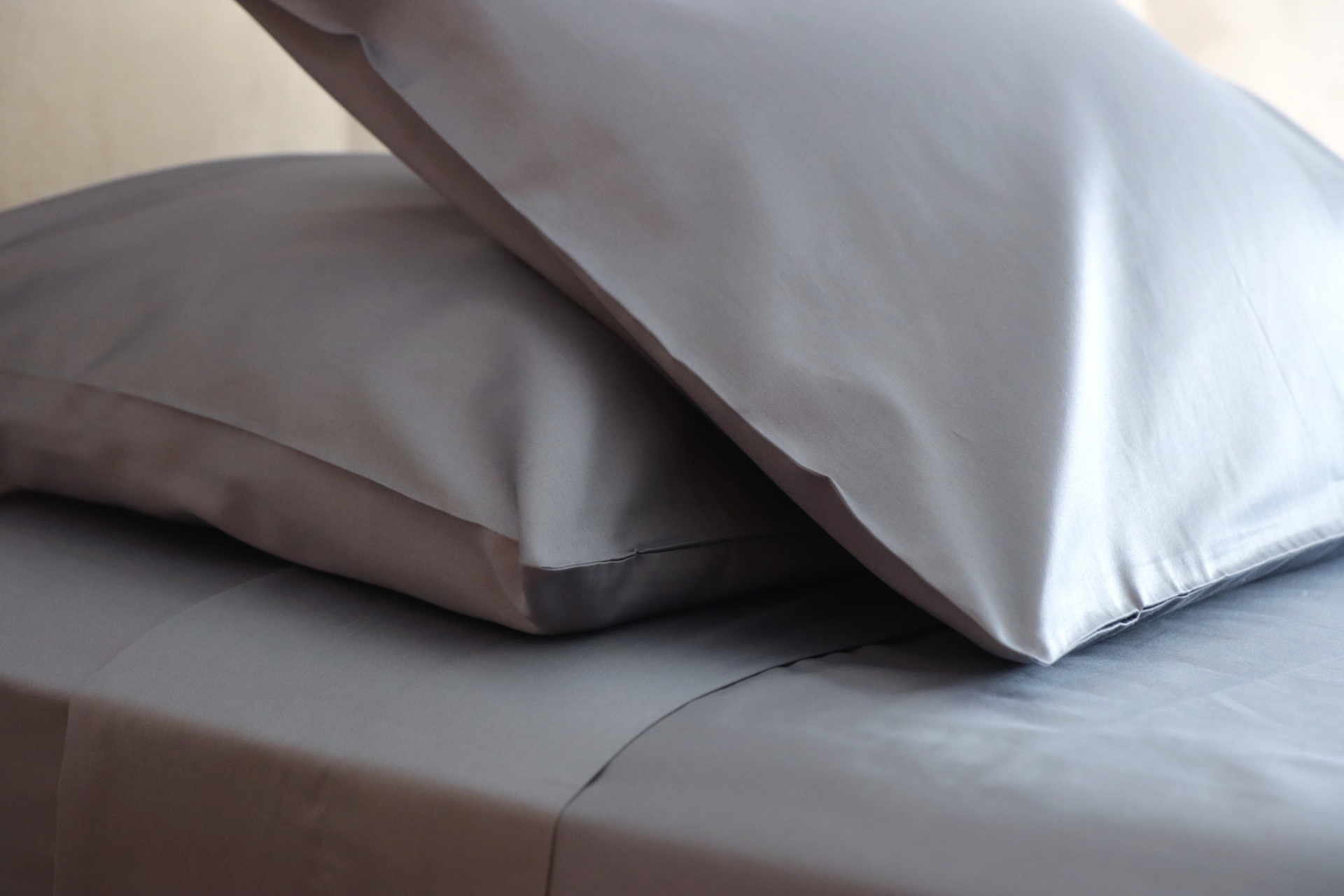 Duas almofadas cinzentas com fronhas lisas sobre lençol cinzento