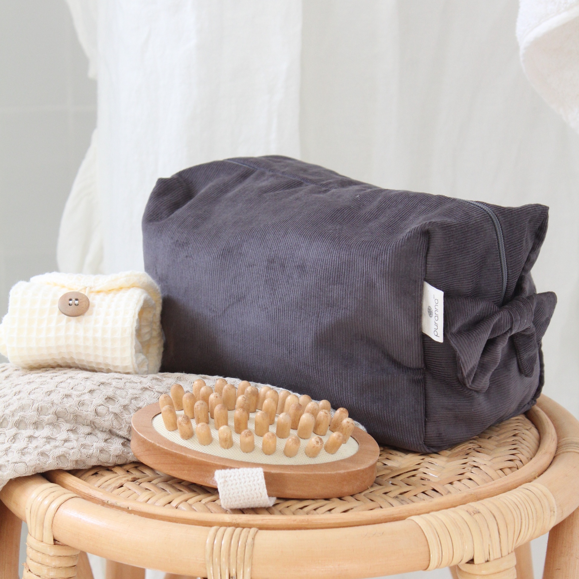 Necessaire cinzenta escura, escova de madeira e panos sobre mesa de vime