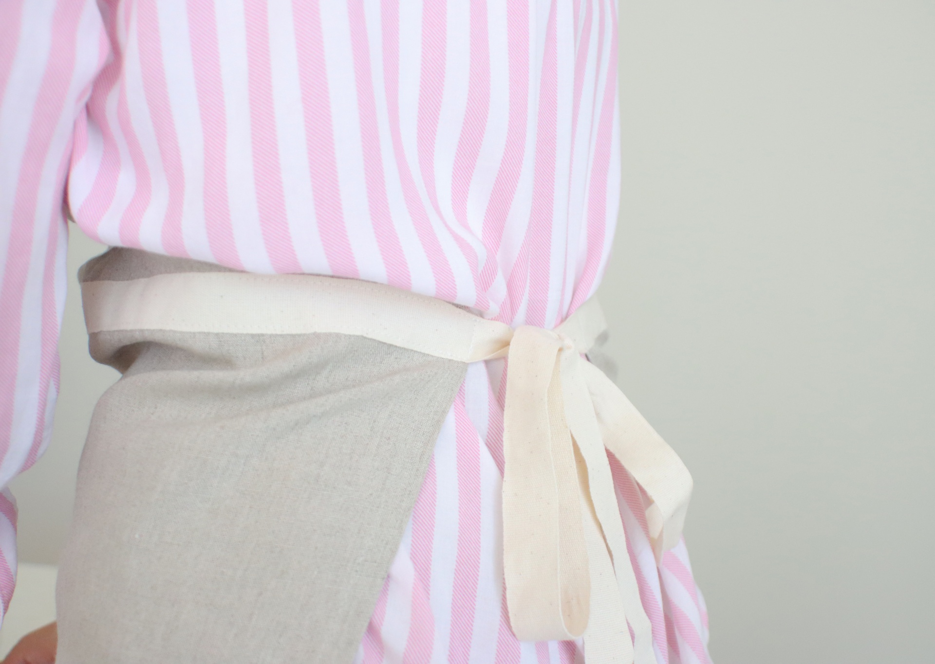Pessoa com camisa riscada rosa e branca e avental cinzento claro com faixa creme