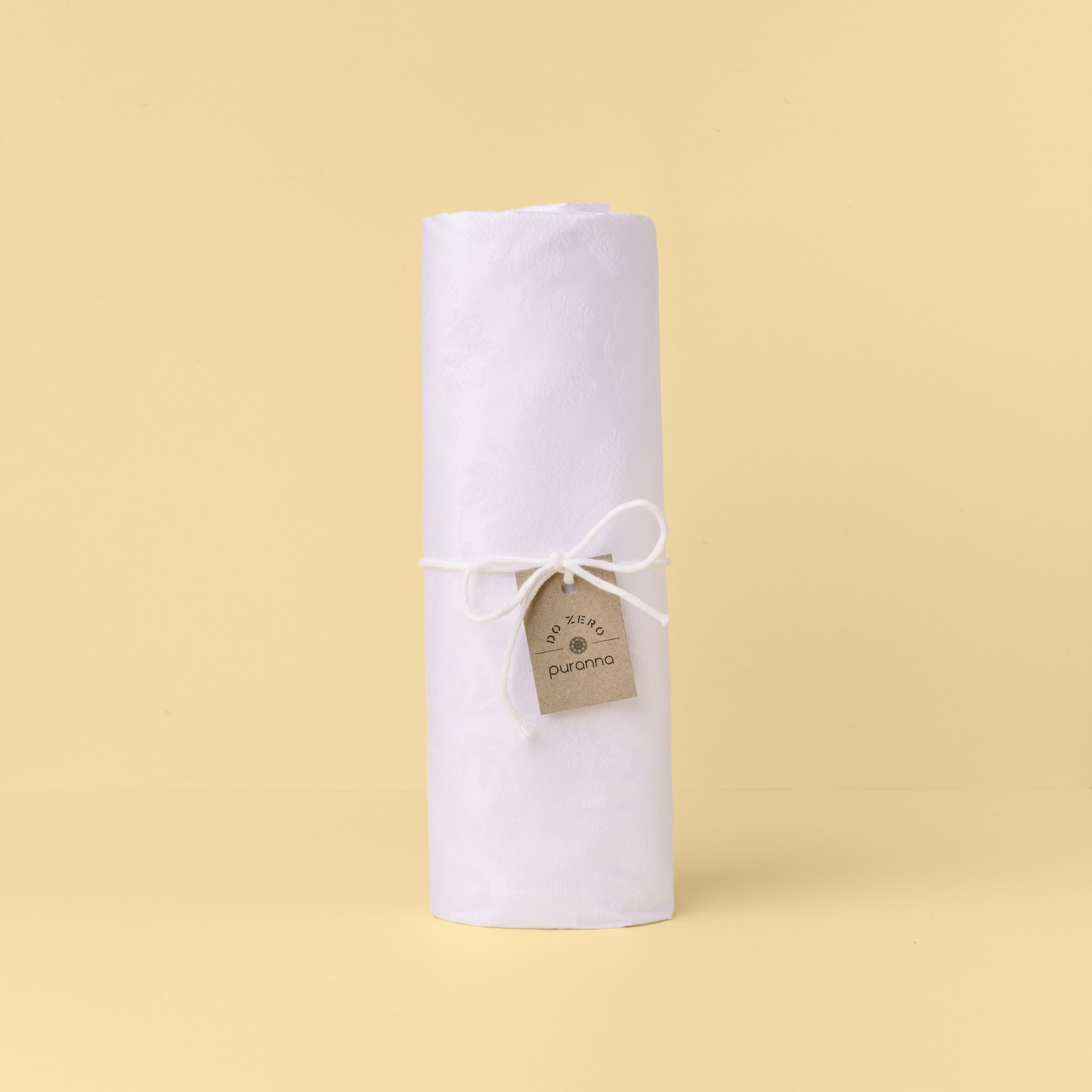 Lençol branco enrolado com etiqueta castanha num fundo creme