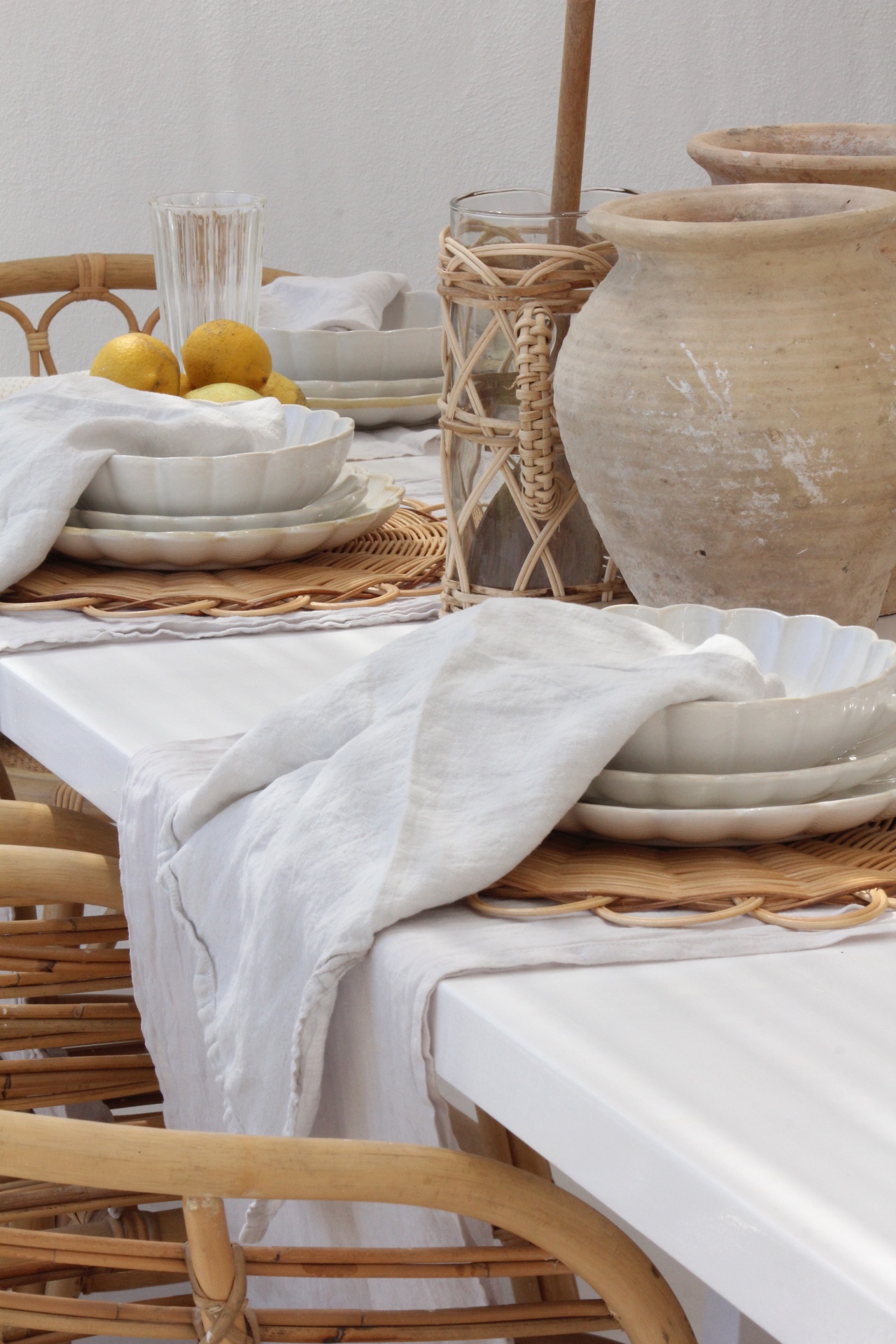 Mesa de jantar com pratos brancos, guardanapos brancos, copo de vidro, jarra de palha e potes de barro