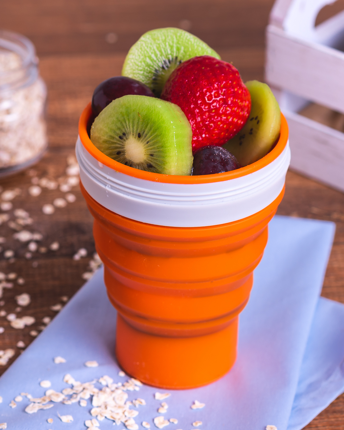 Copo dobrável laranja com frutas frescas em cima de pano azul