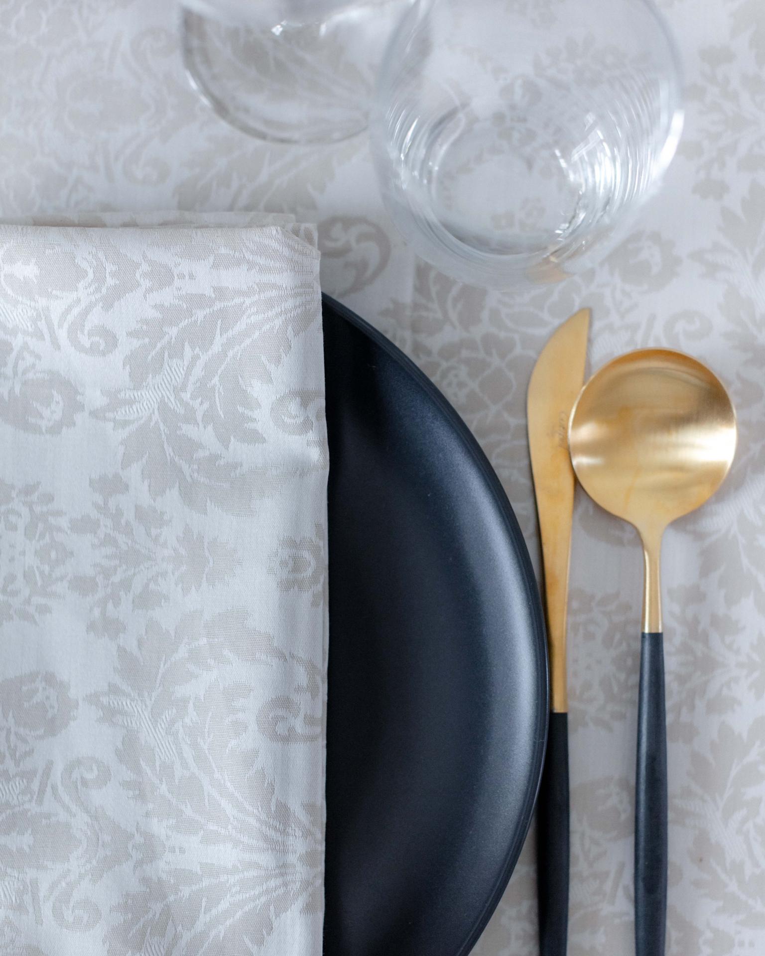 Mesa posta com prato preto, talheres dourados e guardanapo branco