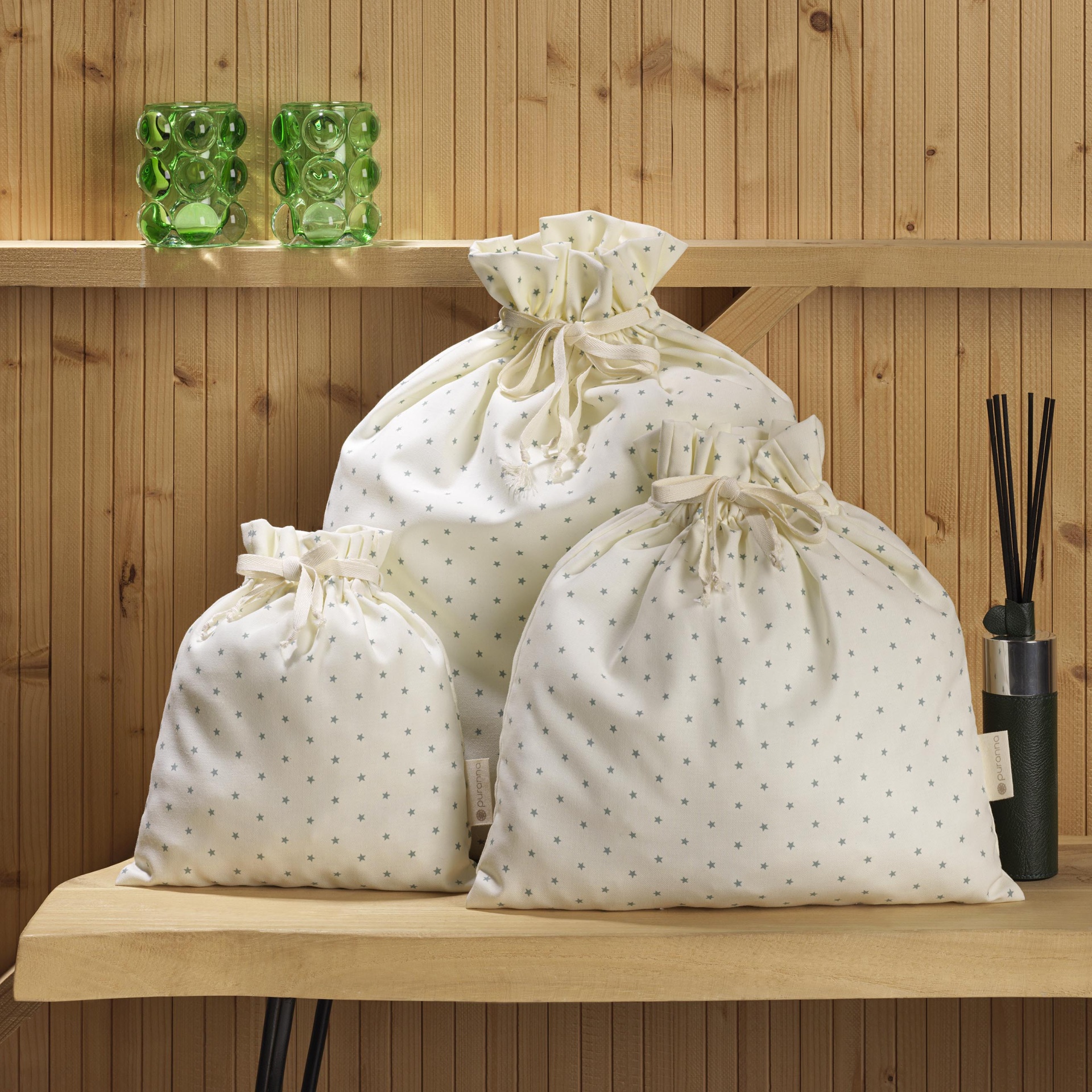Três sacos de tecido branco com padrão de estrelas cinza sobre prateleira de madeira
